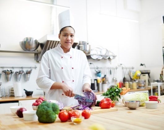 Young woman in chef uniform cooking fresh vegetable salad while cutting purple cabbage